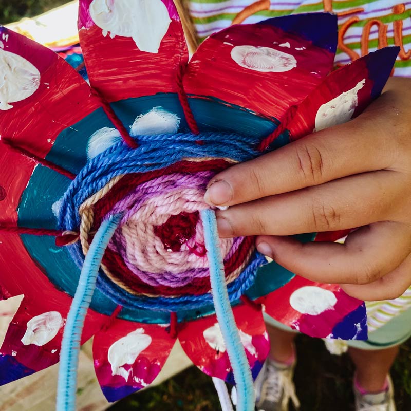 A hand holding a painted and woven craft flower at Festival Flowers workshop at River Fest