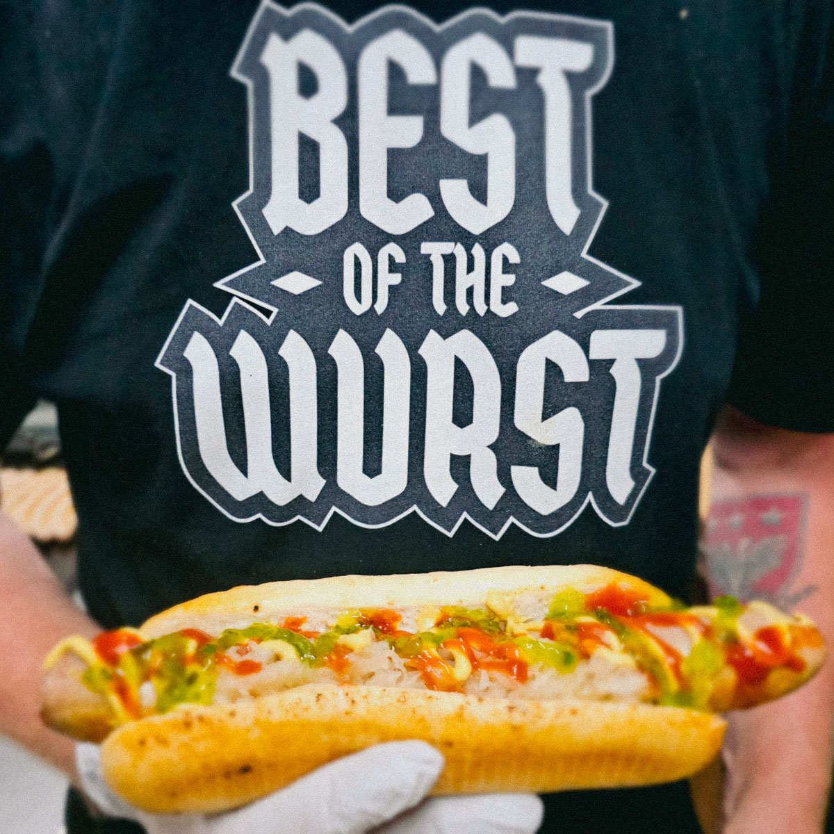 Man holding German Sausage in bun with sauce - Best of the Wurst German Bratwurst