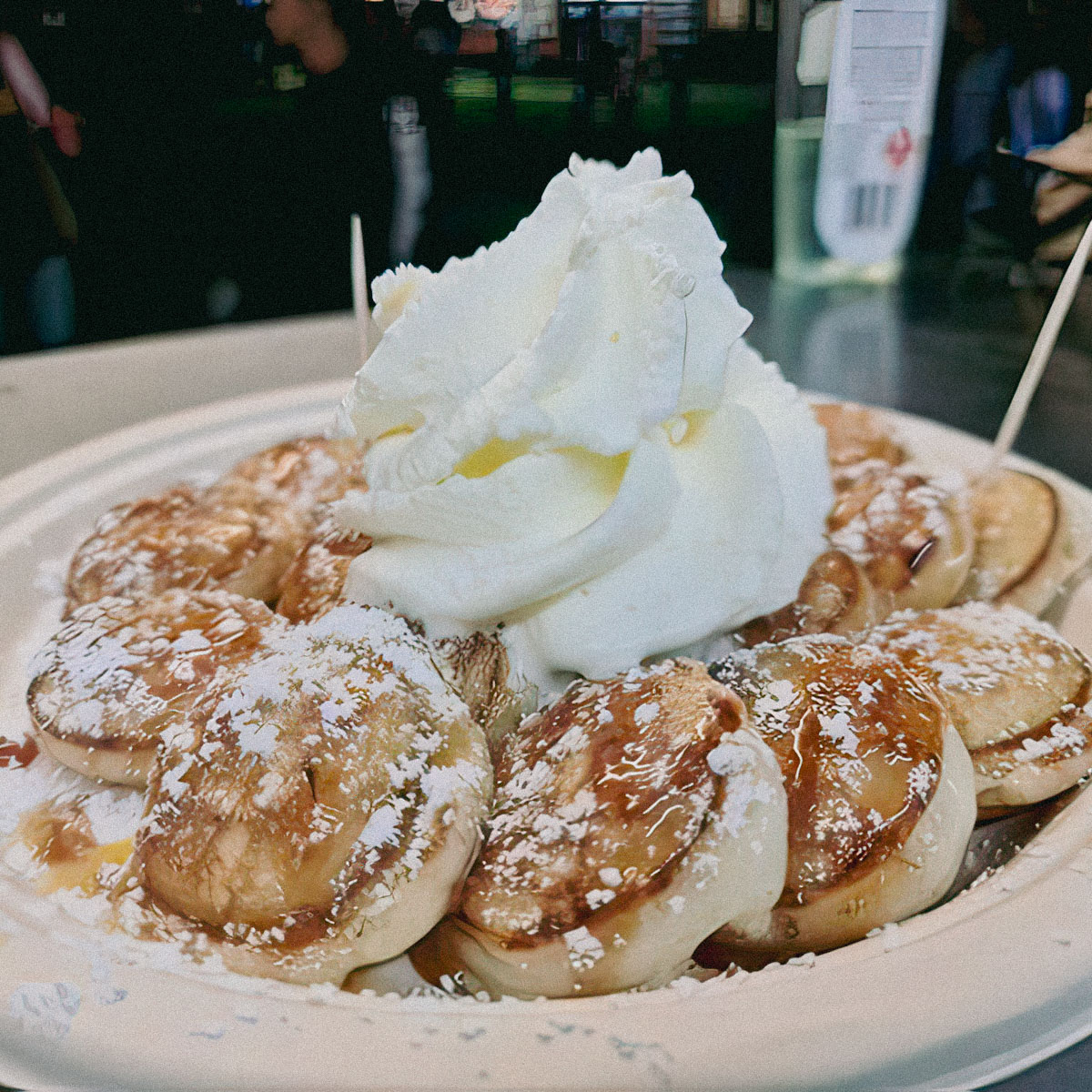 Plate of mini Dutch pancakes on a paper plate with powdered sugar, syrup and ice cream on top